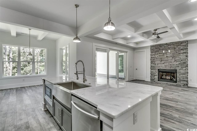 kitchen with hanging light fixtures, a kitchen island with sink, stainless steel dishwasher, light stone countertops, and light hardwood / wood-style floors