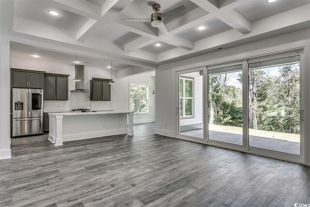 kitchen with stainless steel fridge, wall chimney exhaust hood, beamed ceiling, hardwood / wood-style flooring, and a kitchen island with sink