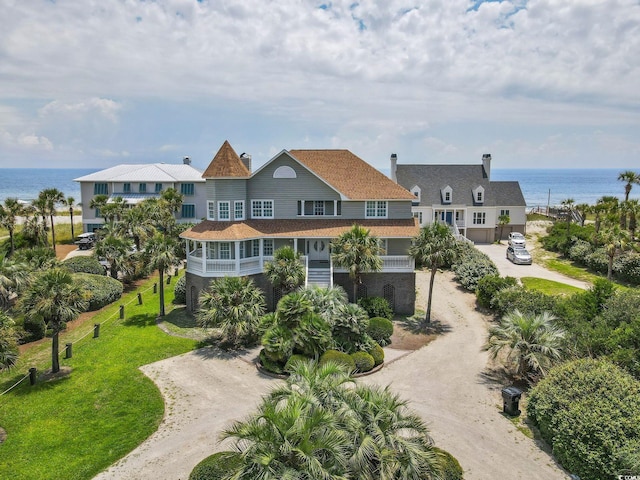 rear view of house featuring dirt driveway, a lawn, and a water view