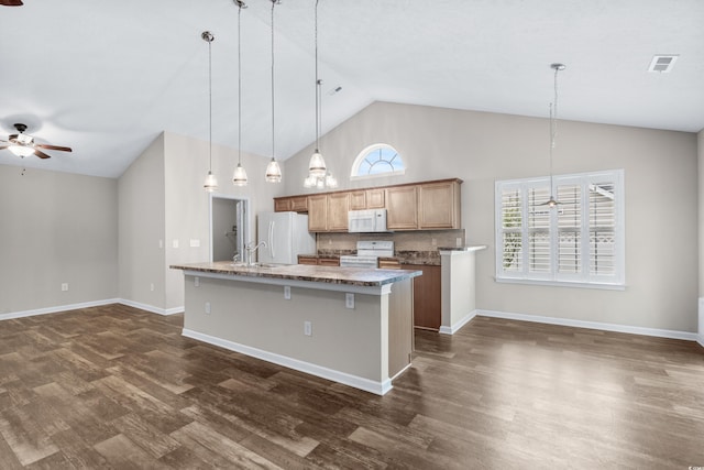 kitchen featuring a kitchen island with sink, hanging light fixtures, white appliances, decorative backsplash, and a breakfast bar