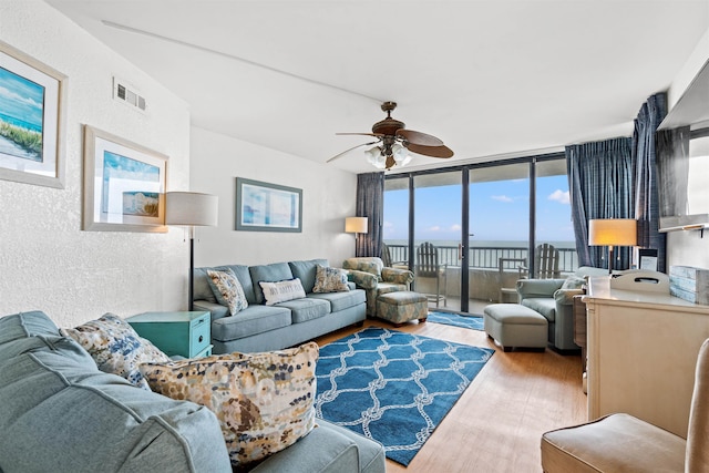 living room with hardwood / wood-style flooring, a wall of windows, and ceiling fan