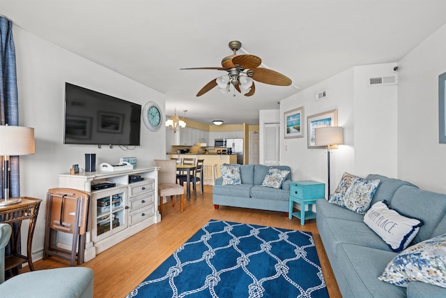 living room featuring ceiling fan with notable chandelier and light hardwood / wood-style flooring