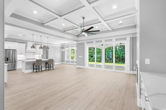 unfurnished living room with crown molding, beam ceiling, ceiling fan with notable chandelier, coffered ceiling, and light hardwood / wood-style floors