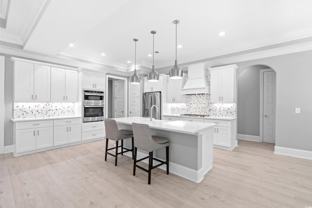 kitchen with custom exhaust hood, white cabinetry, a kitchen breakfast bar, hanging light fixtures, and a kitchen island with sink