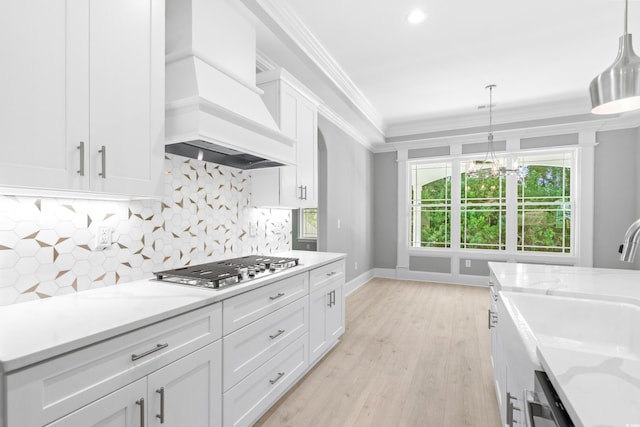 kitchen featuring custom exhaust hood, white cabinetry, light stone counters, and decorative light fixtures