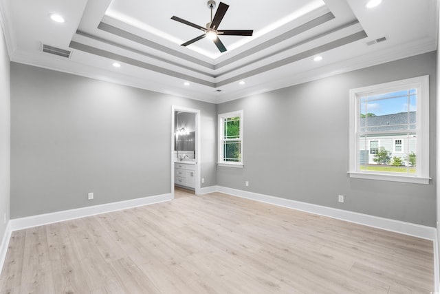 spare room with light wood-type flooring, ceiling fan, a raised ceiling, and ornamental molding