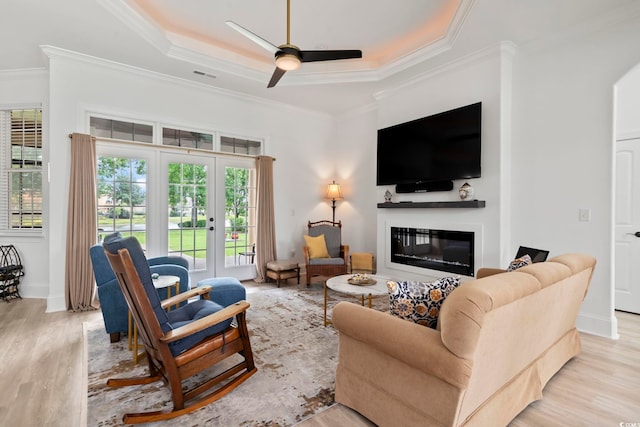 living room with a tray ceiling, light wood-type flooring, ornamental molding, and ceiling fan