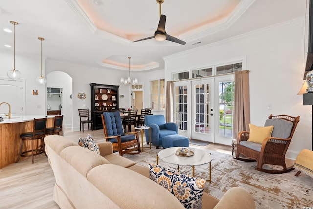 living room with ceiling fan with notable chandelier, a raised ceiling, ornamental molding, and light hardwood / wood-style flooring