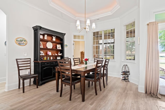 dining area with a tray ceiling, a wealth of natural light, light hardwood / wood-style flooring, and an inviting chandelier