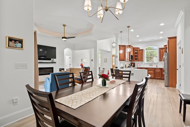 dining area featuring crown molding, ceiling fan with notable chandelier, light wood-type flooring, and a tray ceiling