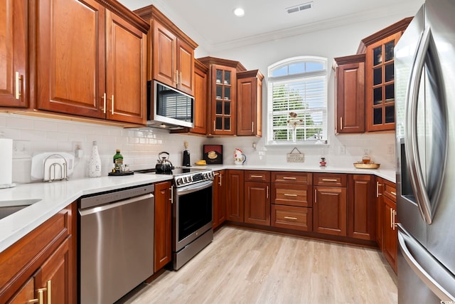 kitchen featuring light wood-type flooring, stainless steel appliances, decorative backsplash, and ornamental molding