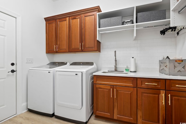 clothes washing area with light wood-type flooring, washer and dryer, cabinets, and sink