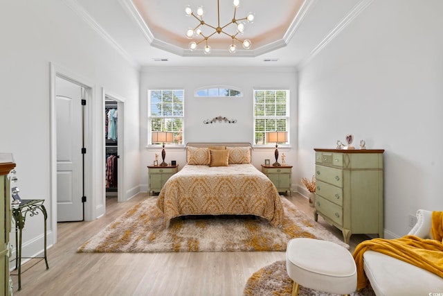 bedroom featuring light hardwood / wood-style floors, a closet, a raised ceiling, a spacious closet, and ornamental molding