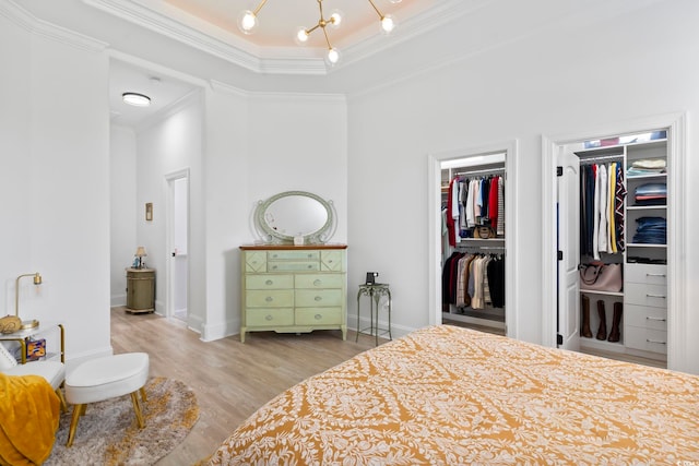 bedroom with a raised ceiling, a closet, ornamental molding, a chandelier, and light wood-type flooring