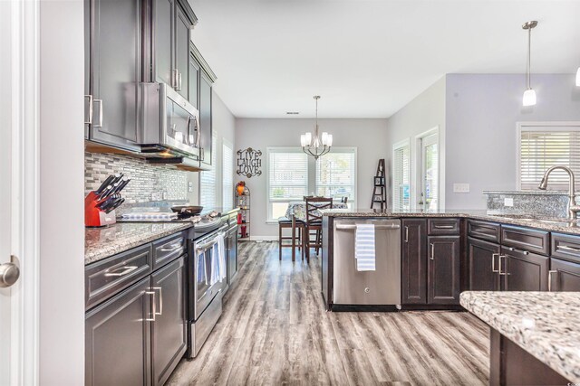 kitchen with appliances with stainless steel finishes, dark brown cabinetry, light stone countertops, pendant lighting, and sink