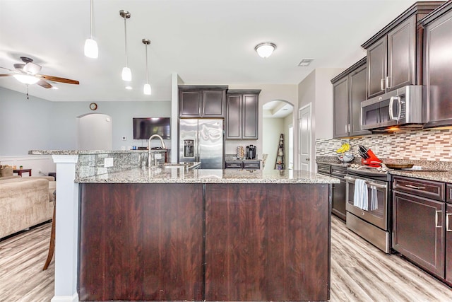 kitchen featuring stainless steel appliances, an island with sink, pendant lighting, light hardwood / wood-style floors, and dark brown cabinets