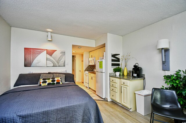 bedroom with light hardwood / wood-style floors, white fridge, and a textured ceiling