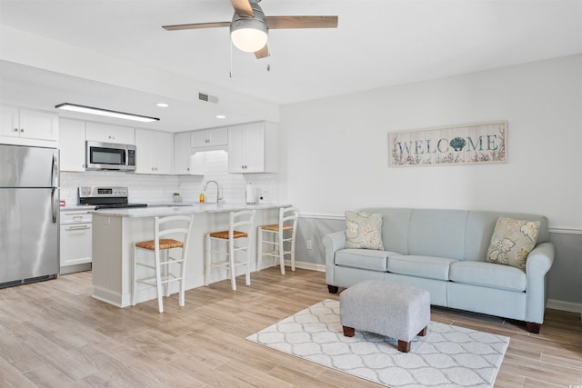 living room featuring sink, light wood-type flooring, and ceiling fan