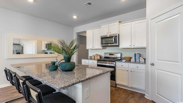 149 Pampa Dr, Loris, SC 29569 - kitchen with appliances with stainless steel finishes, white cabinetry, dark stone countertops, dark hardwood / wood-style flooring, and a kitchen bar