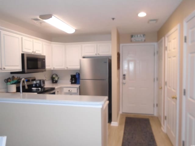 kitchen with kitchen peninsula, light hardwood / wood-style floors, white cabinetry, and stainless steel appliances