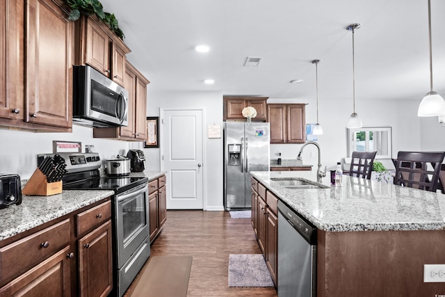 kitchen with stainless steel appliances, a center island with sink, a sink, visible vents, and light stone countertops