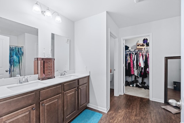 full bath featuring double vanity, wood finished floors, baseboards, and a sink