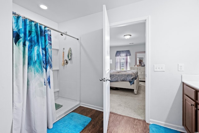 bathroom featuring baseboards, a shower with shower curtain, wood finished floors, and vanity