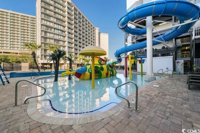 view of swimming pool featuring fence, playground community, a water slide, and a water play area