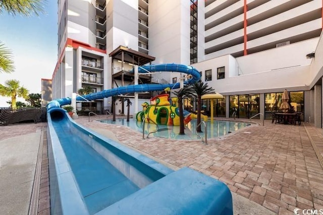 community pool featuring a patio area, fence, a water slide, and a water play area