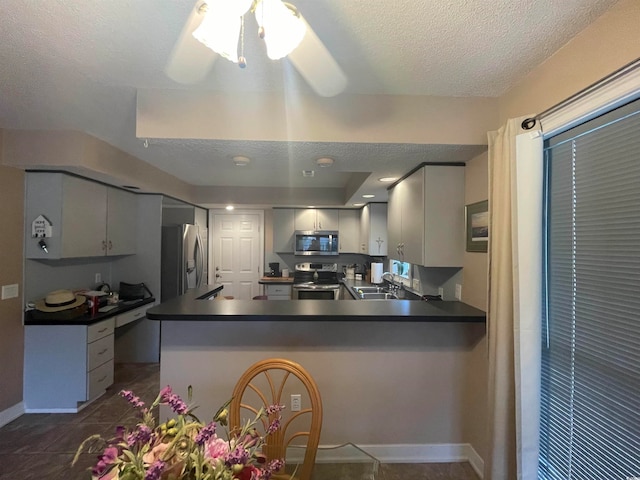 kitchen featuring kitchen peninsula, ceiling fan, stainless steel appliances, dark tile patterned flooring, and sink