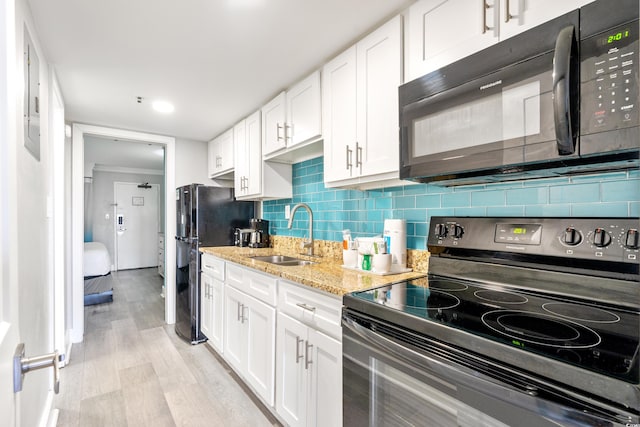 kitchen with light wood-type flooring, backsplash, white cabinets, black appliances, and sink