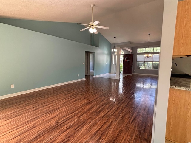 unfurnished living room with a textured ceiling, ceiling fan with notable chandelier, dark wood-type flooring, and high vaulted ceiling