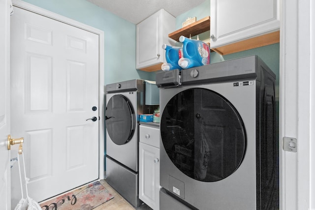 clothes washing area with a textured ceiling, light tile patterned flooring, washing machine and clothes dryer, and cabinets