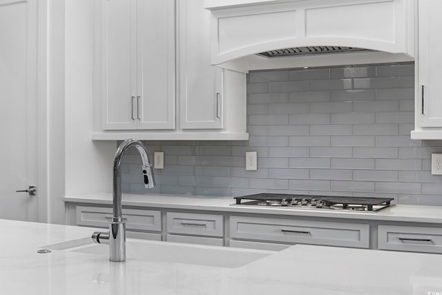 kitchen featuring premium range hood, stainless steel gas stovetop, backsplash, and white cabinetry
