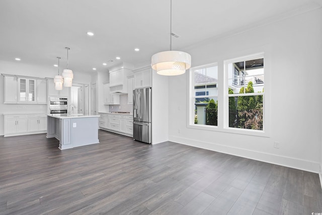 kitchen featuring a center island with sink, white cabinets, decorative light fixtures, and appliances with stainless steel finishes