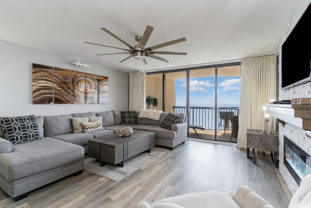 living room featuring ceiling fan, floor to ceiling windows, wood-type flooring, and a stone fireplace