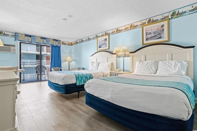 bedroom featuring a wall unit AC, access to outside, a textured ceiling, and light wood-type flooring