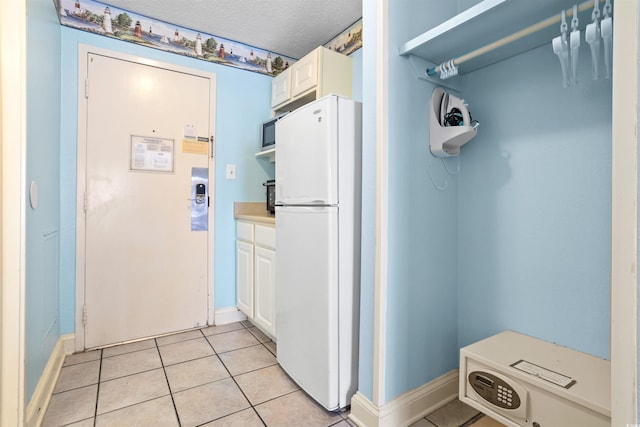 kitchen with a textured ceiling, light tile patterned floors, white fridge, and white cabinets