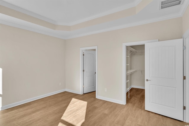 unfurnished bedroom featuring a walk in closet, a closet, light hardwood / wood-style floors, and ornamental molding