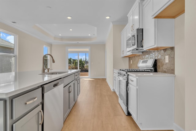 kitchen featuring sink, appliances with stainless steel finishes, a kitchen island with sink, white cabinets, and ornamental molding