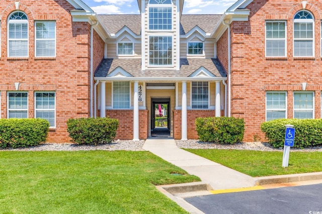 multi unit property with a shingled roof, a front yard, and brick siding