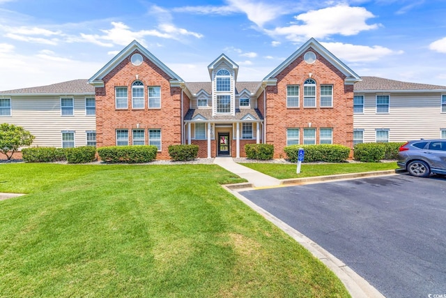 townhome / multi-family property featuring a front yard, brick siding, and uncovered parking