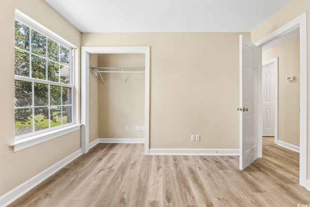 unfurnished bedroom with light wood-style flooring, a closet, baseboards, and multiple windows