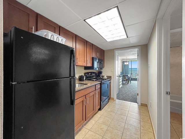 kitchen with stone countertops, light tile patterned floors, a drop ceiling, and black appliances