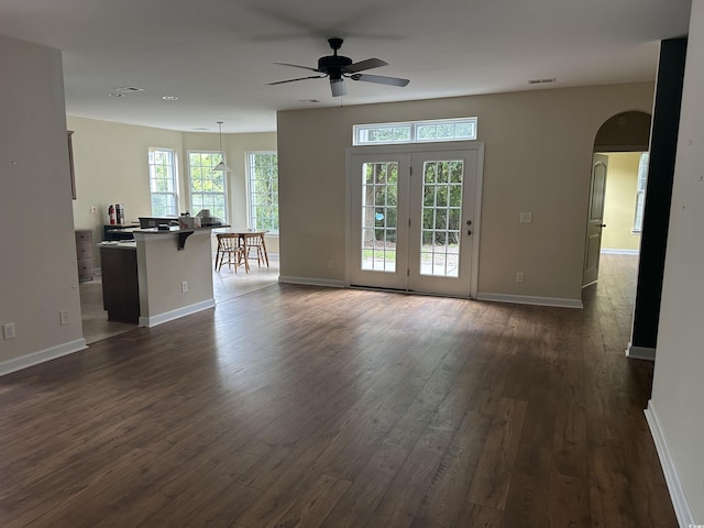 unfurnished living room featuring arched walkways, visible vents, dark wood-style flooring, and baseboards