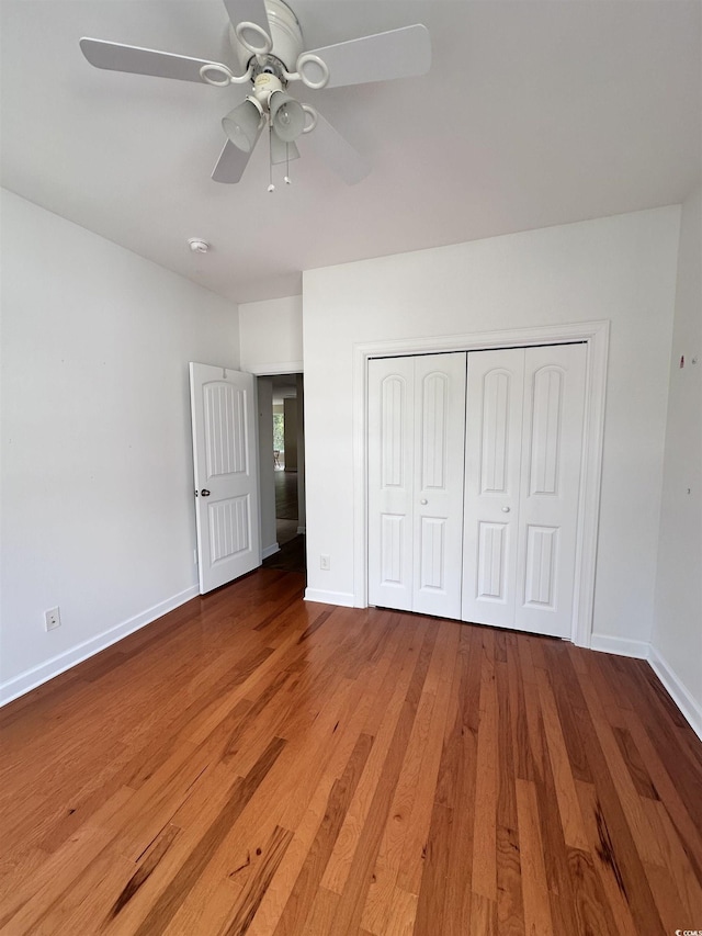 unfurnished bedroom featuring wood finished floors, baseboards, a closet, and ceiling fan