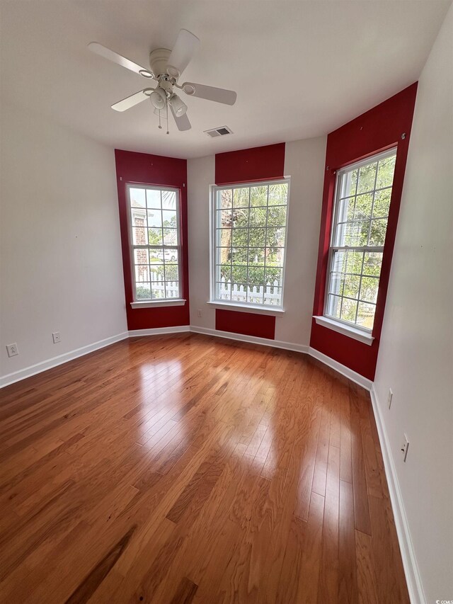 spare room with a ceiling fan, hardwood / wood-style flooring, baseboards, and visible vents