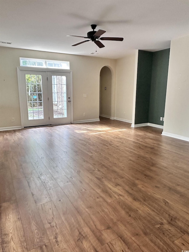 spare room with visible vents, a ceiling fan, hardwood / wood-style flooring, arched walkways, and baseboards