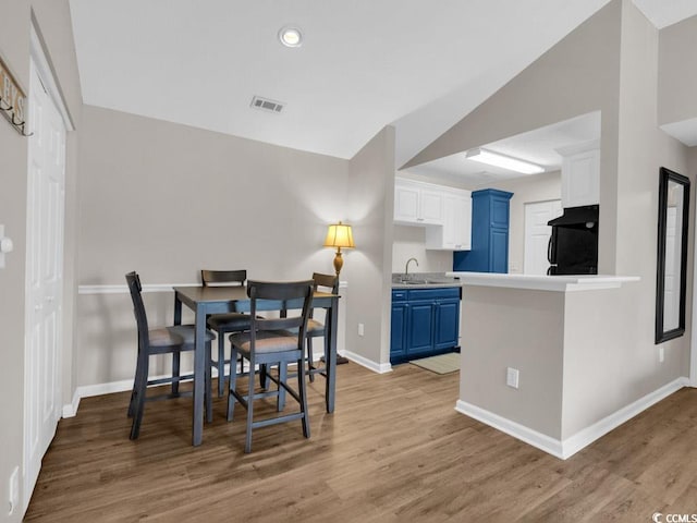 dining room with light hardwood / wood-style flooring, vaulted ceiling, and sink