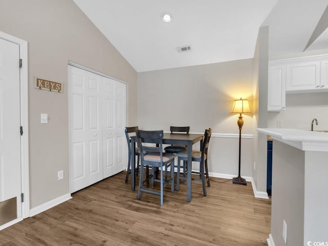 dining room with lofted ceiling, sink, and light hardwood / wood-style flooring